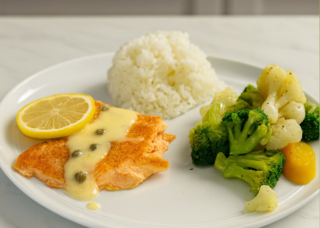 Plate of food with salmon, rice, broccoli, and lemon on a kitchen counter.